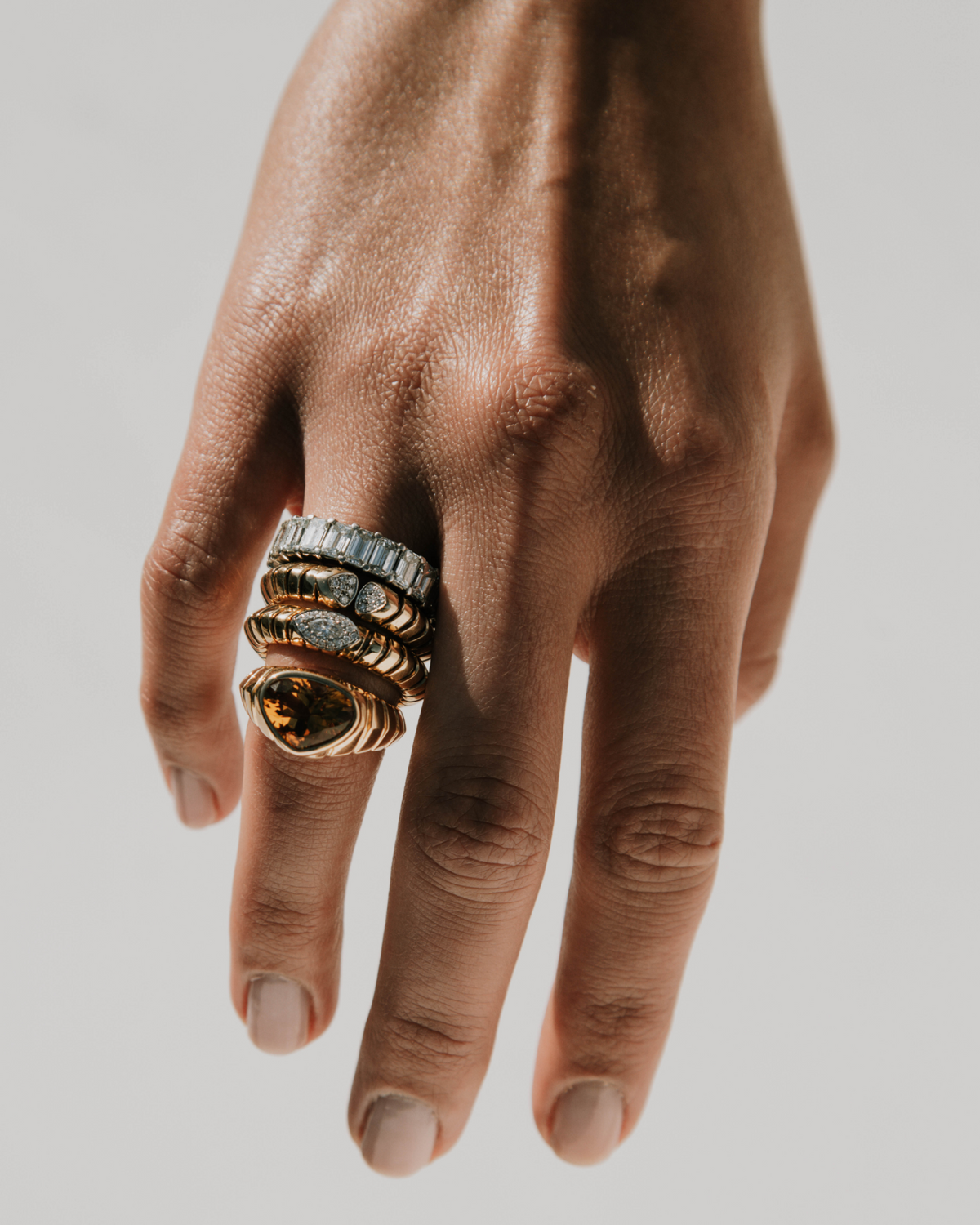 Hand wearing multiple rings on a neutral background