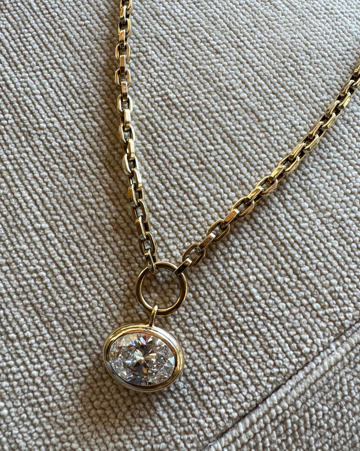 Gold necklace with a diamond pendant on a textured beige surface